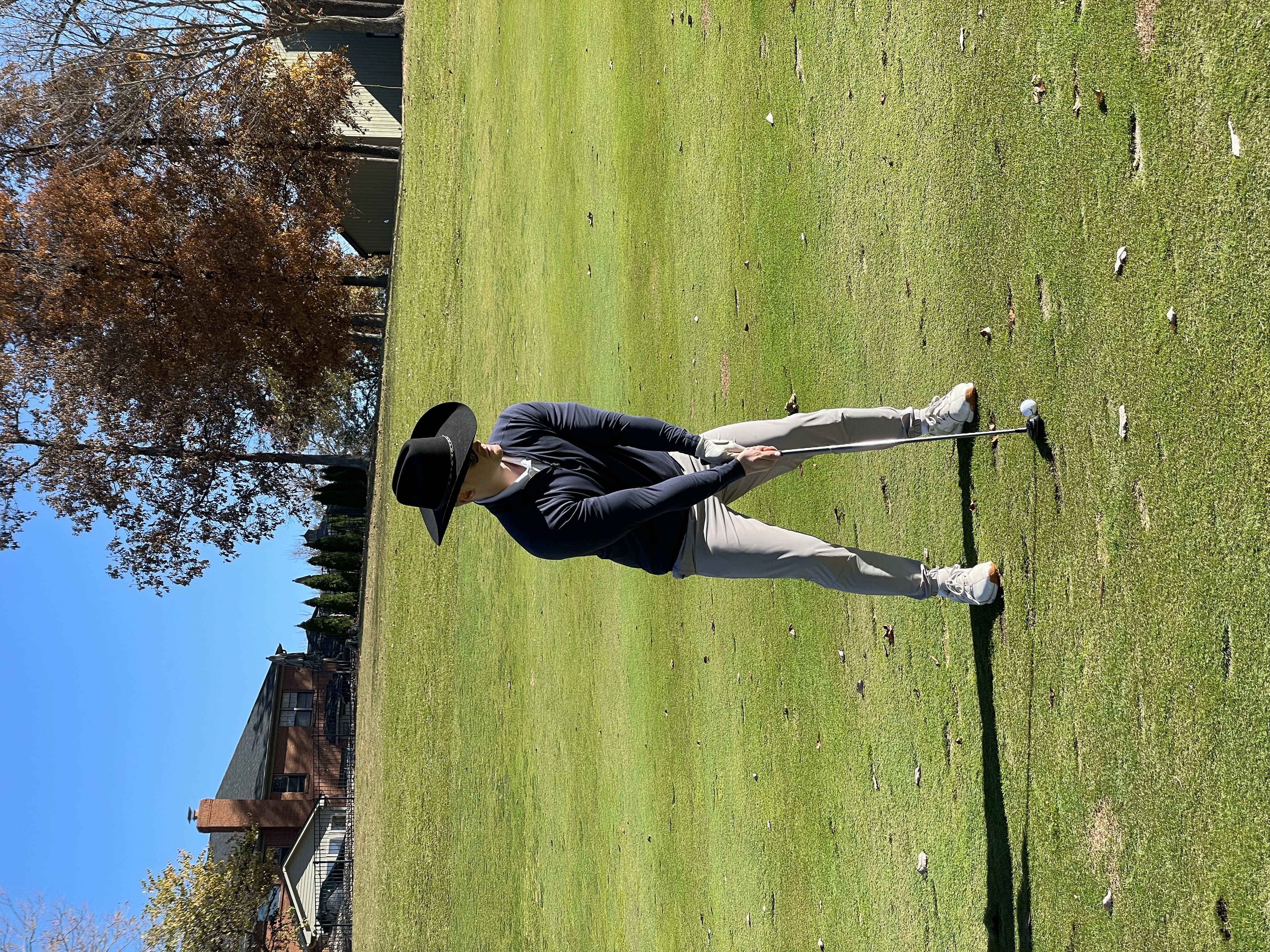 Golfer addressing the ball on a sunny fairway while wearing a wide-brim hat.